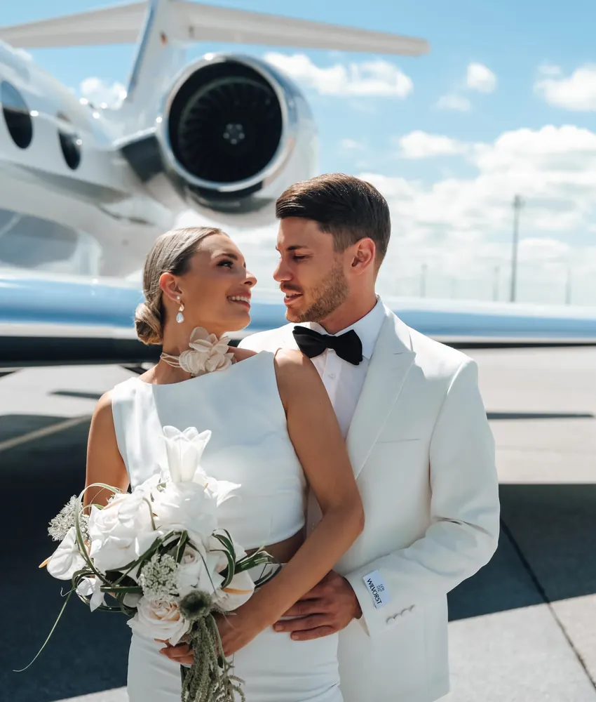 Gestylte Braut mit Bräutigam vor dem Flugzeug, Brautstyling für eine Hochzeit im Ausland